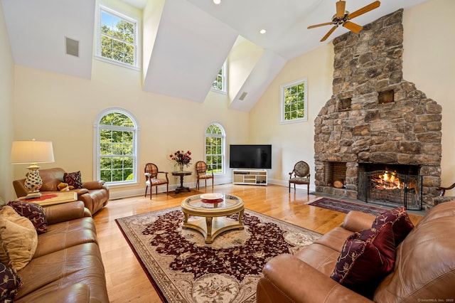 living room with ceiling fan, light hardwood / wood-style floors, a towering ceiling, and a fireplace