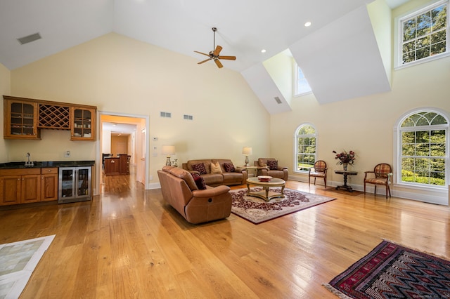 living room featuring light hardwood / wood-style floors, wet bar, a towering ceiling, and beverage cooler