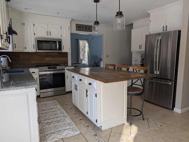 kitchen featuring appliances with stainless steel finishes, a kitchen breakfast bar, white cabinets, wood counters, and a sink