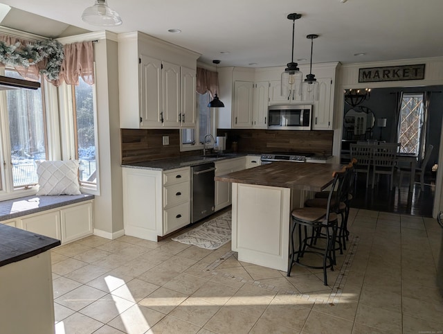 kitchen featuring decorative light fixtures, butcher block counters, decorative backsplash, stainless steel appliances, and a sink