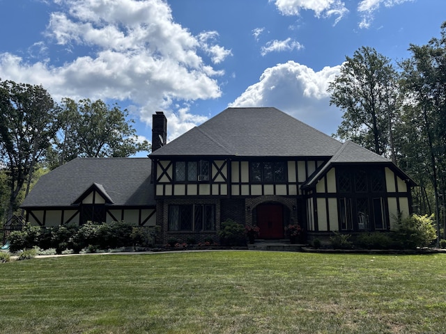 view of front facade with brick siding, a lawn, a chimney, and roof with shingles