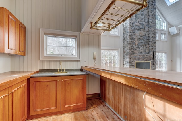 kitchen with brown cabinetry, a sink, lofted ceiling with skylight, a fireplace, and light wood-style flooring