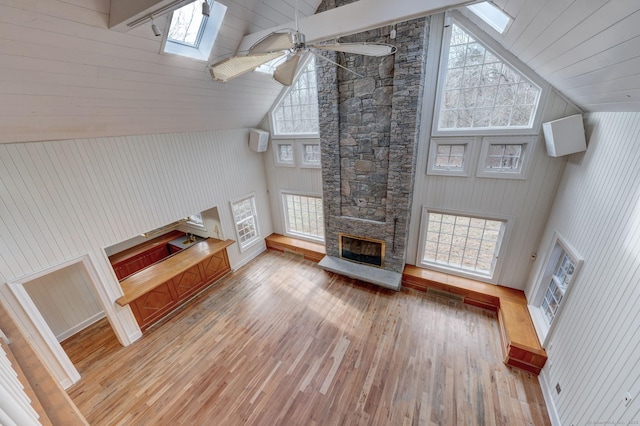 unfurnished living room featuring a stone fireplace, a skylight, light wood-style flooring, high vaulted ceiling, and ceiling fan