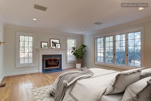 bedroom featuring ornamental molding, a high end fireplace, and light hardwood / wood-style flooring