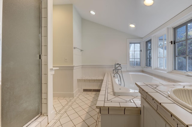 bathroom featuring tile patterned flooring, vanity, a relaxing tiled tub, and lofted ceiling