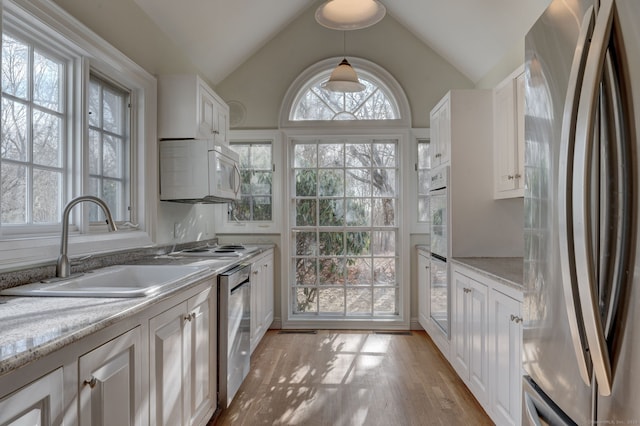 kitchen with stainless steel appliances, vaulted ceiling, sink, decorative light fixtures, and white cabinets