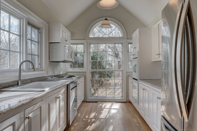 kitchen featuring white cabinets, stainless steel appliances, a sink, light wood-type flooring, and lofted ceiling
