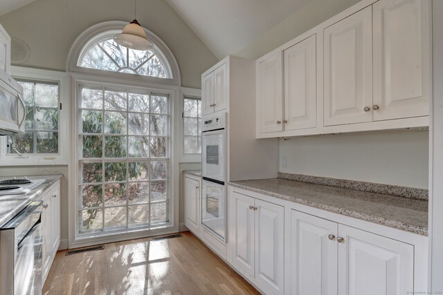 kitchen featuring light wood finished floors, white double oven, white cabinets, lofted ceiling, and visible vents