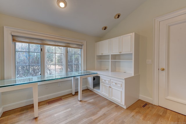 unfurnished office with light wood-type flooring, vaulted ceiling, and built in desk