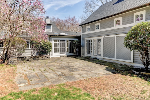 rear view of property with a patio area, a chimney, and roof with shingles