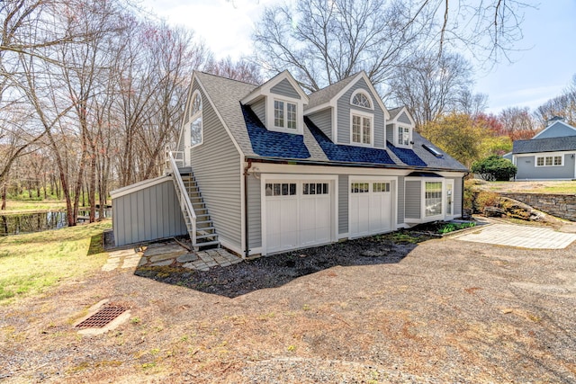 view of home's exterior with a shingled roof, stairs, dirt driveway, and a garage