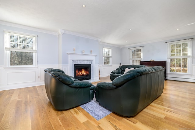 living room with a high end fireplace, a healthy amount of sunlight, light hardwood / wood-style flooring, and ornamental molding