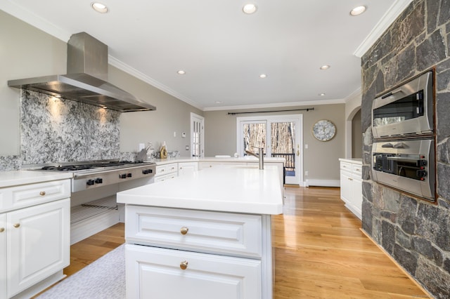 kitchen featuring ornamental molding, stainless steel appliances, a kitchen island with sink, light hardwood / wood-style floors, and range hood