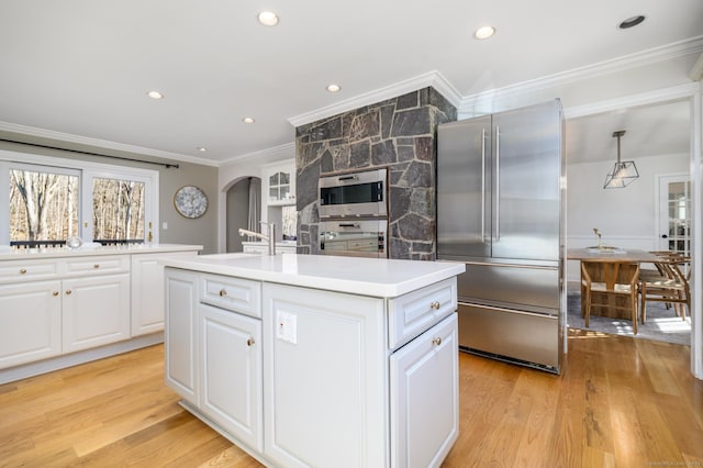 kitchen featuring white cabinets, stainless steel appliances, hanging light fixtures, and an island with sink