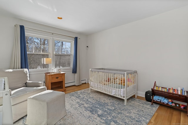 bedroom featuring a baseboard heating unit, hardwood / wood-style flooring, and a nursery area