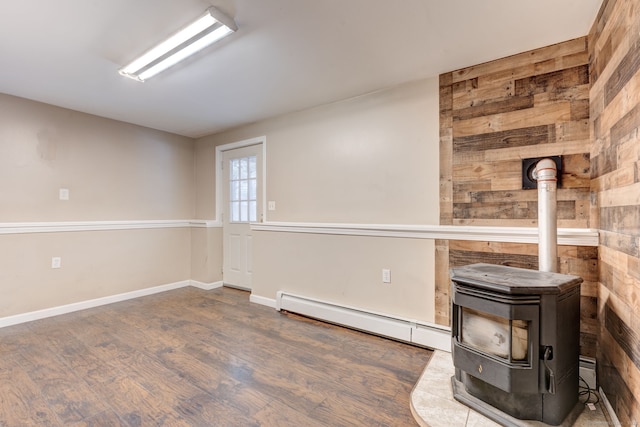 basement featuring a wood stove, a baseboard heating unit, and dark hardwood / wood-style floors