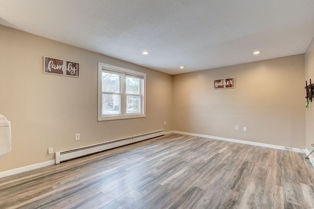 unfurnished room with light hardwood / wood-style floors, baseboard heating, and a textured ceiling