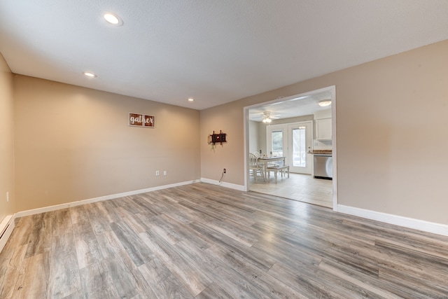 spare room featuring baseboard heating, light wood-type flooring, and ceiling fan