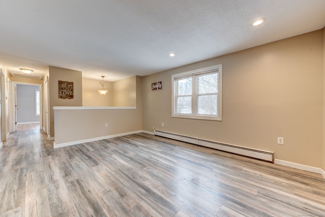 empty room featuring a textured ceiling, baseboard heating, and light hardwood / wood-style flooring