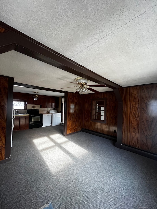 unfurnished living room with a textured ceiling, wood walls, carpet flooring, washing machine and clothes dryer, and beamed ceiling