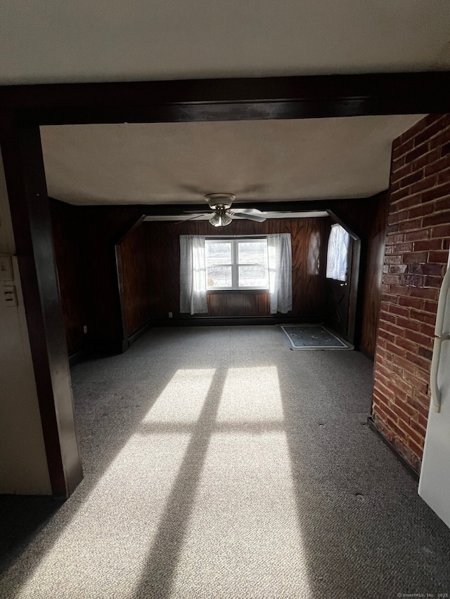 empty room featuring ceiling fan, wooden walls, beamed ceiling, and light carpet