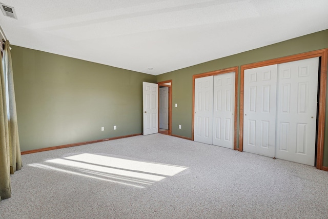 unfurnished bedroom featuring carpet flooring, two closets, and a textured ceiling