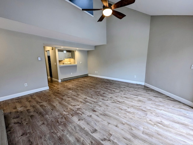 unfurnished living room featuring a towering ceiling, light hardwood / wood-style flooring, ceiling fan, and baseboard heating