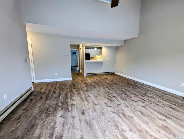 unfurnished living room with wood-type flooring, a high ceiling, and a baseboard heating unit