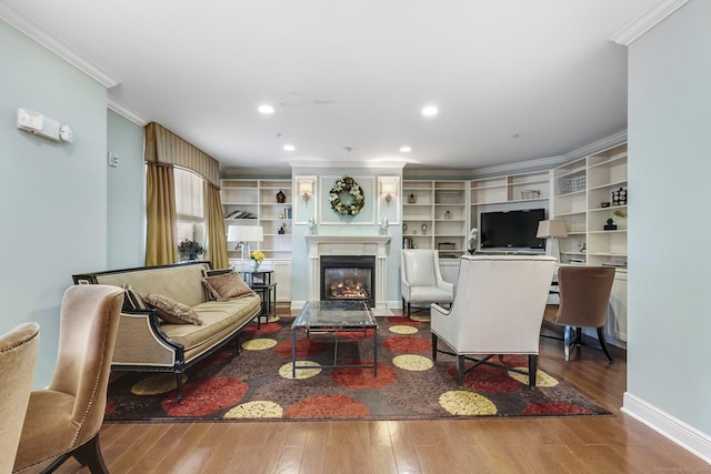 living area with wood finished floors, baseboards, recessed lighting, a glass covered fireplace, and crown molding