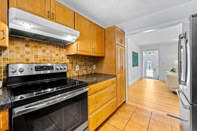 kitchen with dark stone countertops, stainless steel appliances, light tile patterned flooring, and backsplash