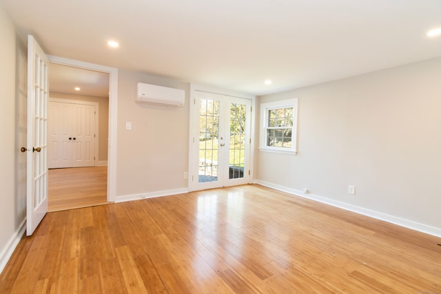 unfurnished room featuring a wall mounted air conditioner, light wood-type flooring, and french doors