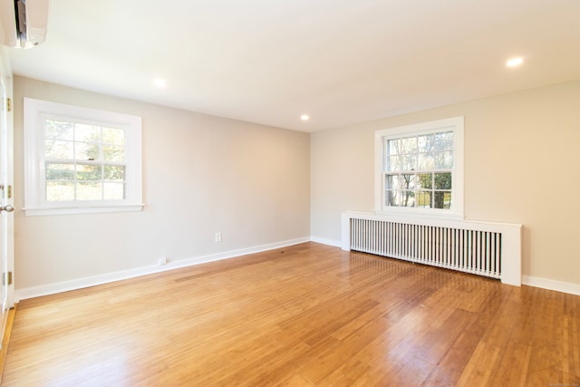 empty room featuring a wall mounted AC, radiator, and light wood-type flooring