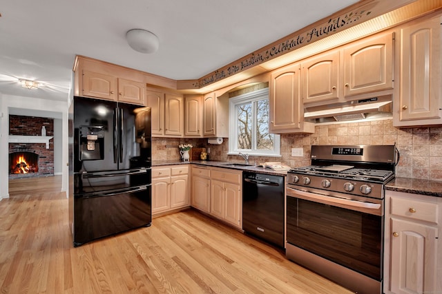 kitchen with sink, a brick fireplace, dark stone countertops, light hardwood / wood-style floors, and black appliances