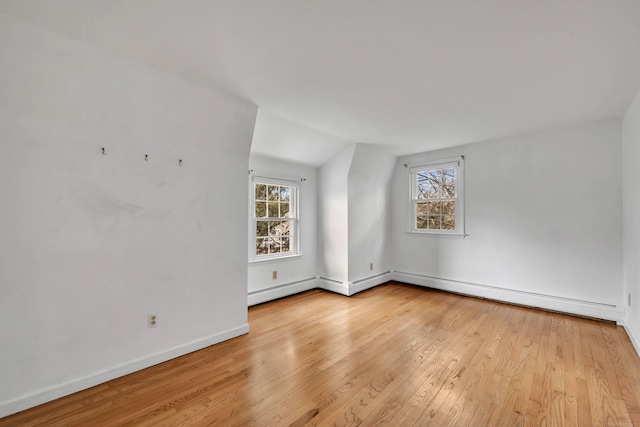 empty room with vaulted ceiling, a baseboard radiator, and light hardwood / wood-style flooring