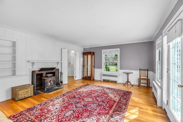 living room featuring radiator, built in shelves, a wood stove, crown molding, and hardwood / wood-style flooring