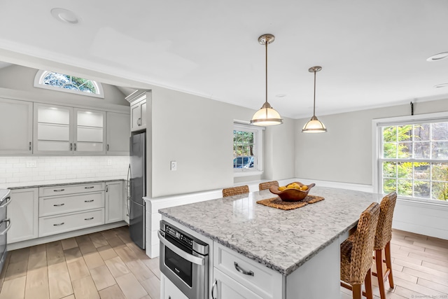 kitchen featuring decorative backsplash, appliances with stainless steel finishes, light stone countertops, light hardwood / wood-style flooring, and a kitchen island