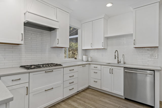 kitchen with appliances with stainless steel finishes, white cabinetry, tasteful backsplash, sink, and custom range hood