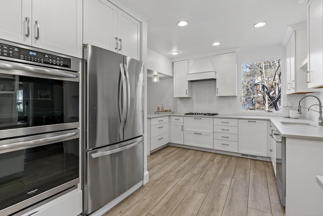 kitchen featuring tasteful backsplash, custom exhaust hood, sink, white cabinetry, and appliances with stainless steel finishes