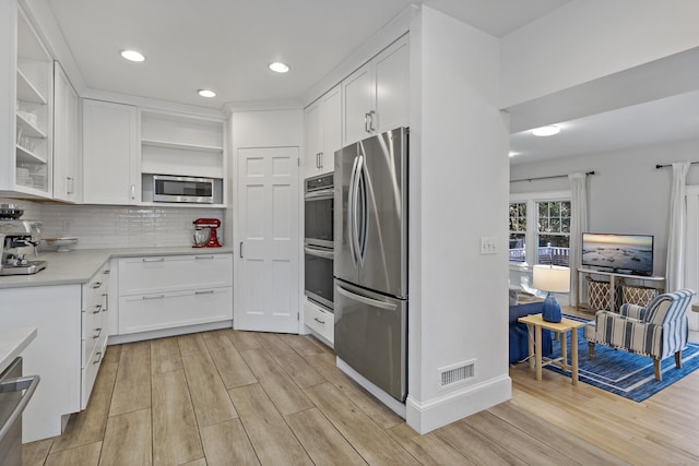 kitchen featuring tasteful backsplash, white cabinets, stainless steel appliances, and light hardwood / wood-style floors