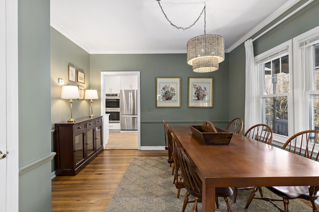 dining space with an inviting chandelier, ornamental molding, and light hardwood / wood-style flooring