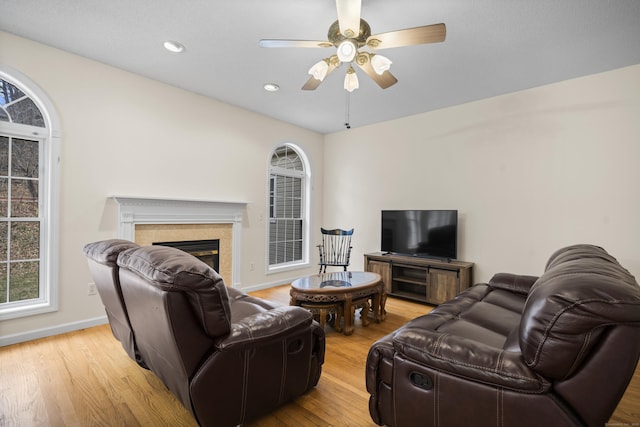 living room with ceiling fan, light hardwood / wood-style floors, and a tile fireplace