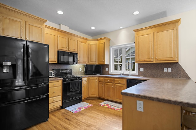 kitchen featuring kitchen peninsula, light wood-type flooring, backsplash, sink, and black appliances