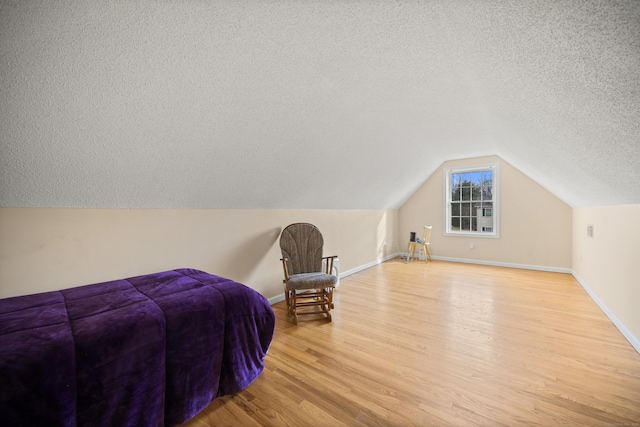 bedroom featuring light wood-type flooring, a textured ceiling, and vaulted ceiling