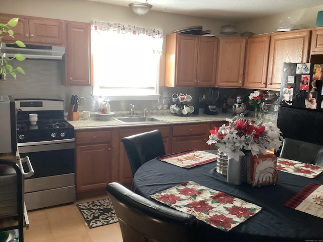 kitchen featuring ventilation hood, black fridge, stainless steel range with gas cooktop, sink, and light tile patterned flooring