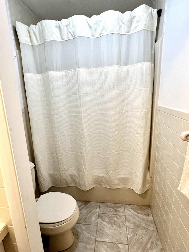 bathroom with tile walls, toilet, and shower / tub combo with curtain