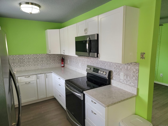 kitchen with decorative backsplash, appliances with stainless steel finishes, light stone counters, dark wood-type flooring, and white cabinets