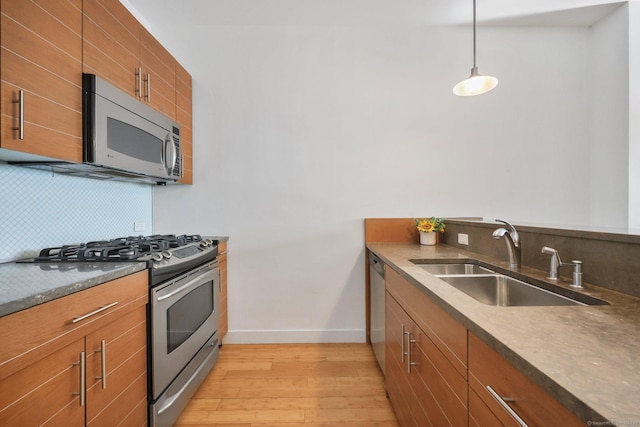 kitchen featuring appliances with stainless steel finishes, tasteful backsplash, sink, hanging light fixtures, and light hardwood / wood-style flooring