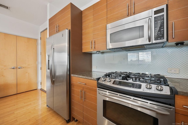 kitchen featuring dark stone countertops, decorative backsplash, light wood-type flooring, and appliances with stainless steel finishes