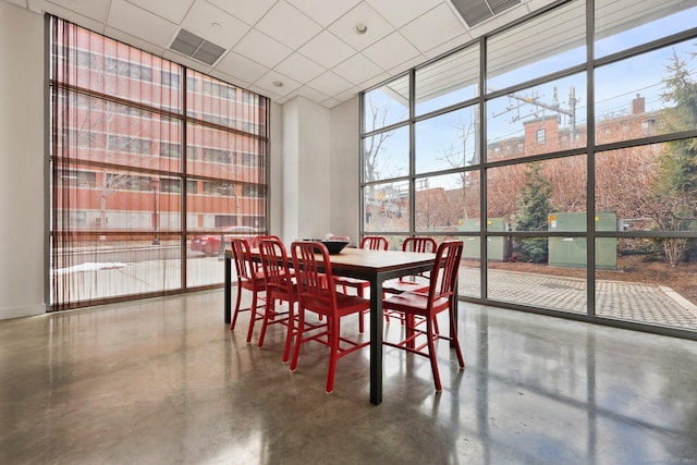 dining space featuring a paneled ceiling, concrete floors, and expansive windows