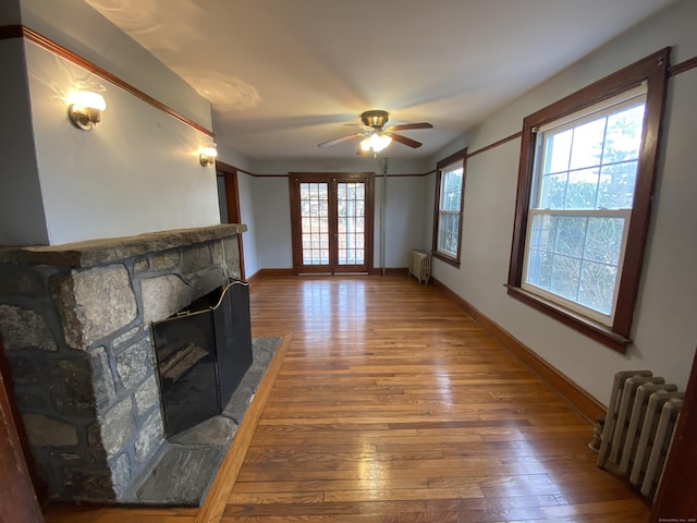 unfurnished living room with radiator, ceiling fan, a fireplace, and hardwood / wood-style flooring